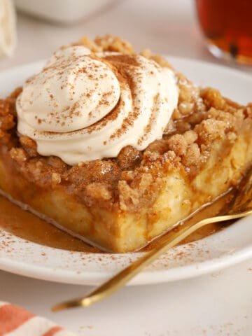 Slice of pumpkin french toast casserole on a white plate topped with whipped cream and cinnamon