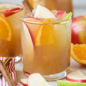 Sangria in a glass garnished with sliced apples, oranges, and cinnamon sticks.