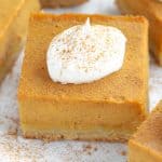 Square slice of pumpkin pie topped with whipped cream.