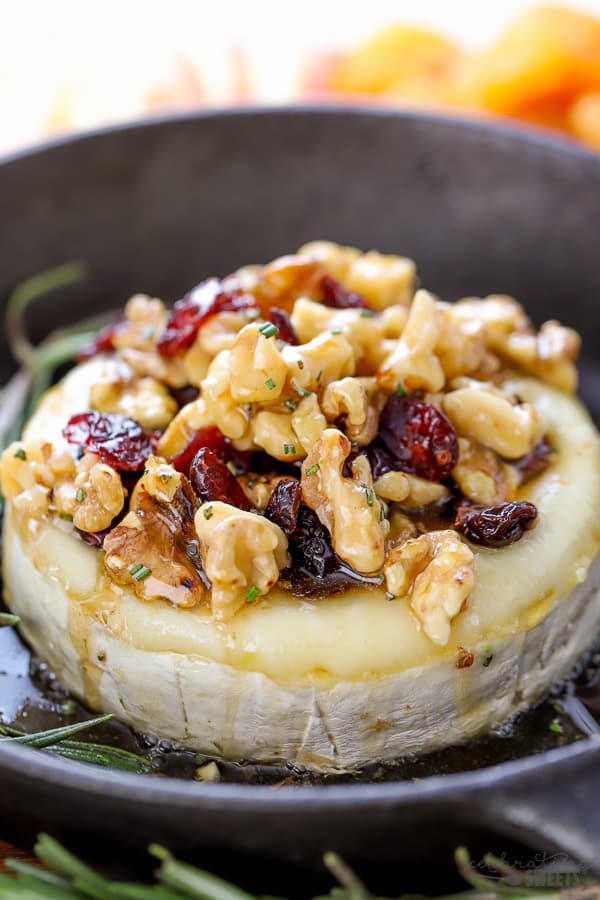 Wheel of brie cheese topped with dried cranberries and walnuts.