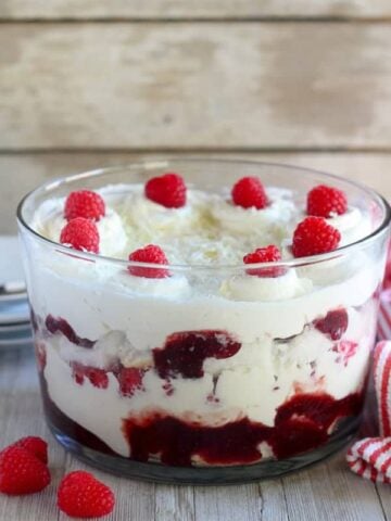 Trifle dish with cake, whipped cream, jam and raspberries.