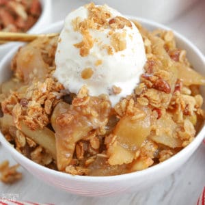 Apple crisp in a white bowl topped with ice cream