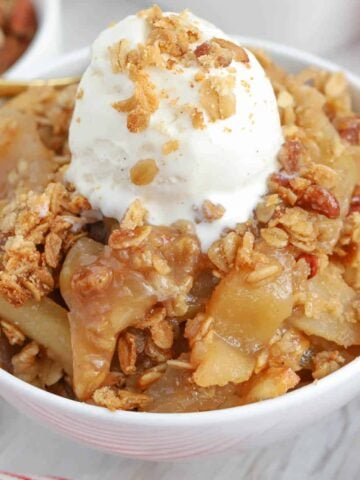 Apple crisp in a white bowl topped with ice cream