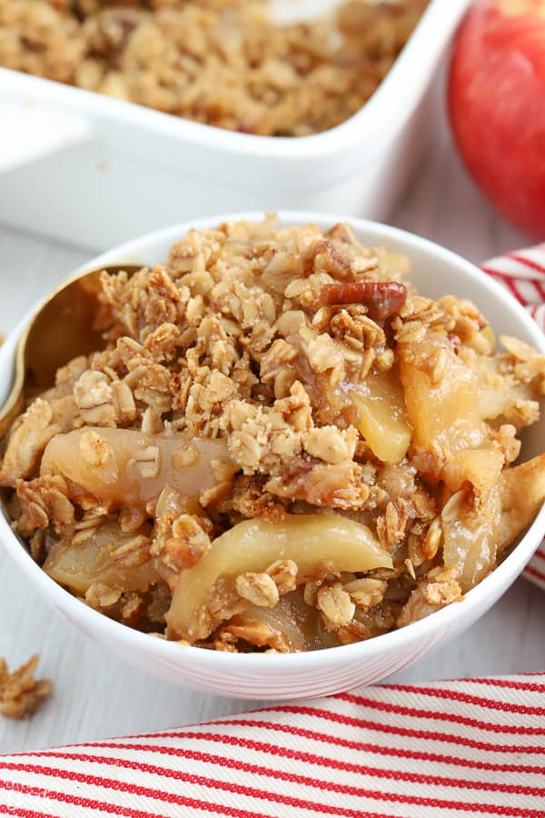 Apple crisp in a white bowl next to a red and white striped napkin