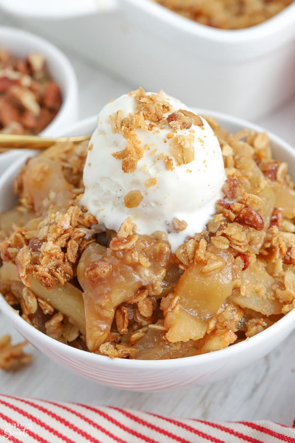 Apple crisp in a white bowl topped with ice cream