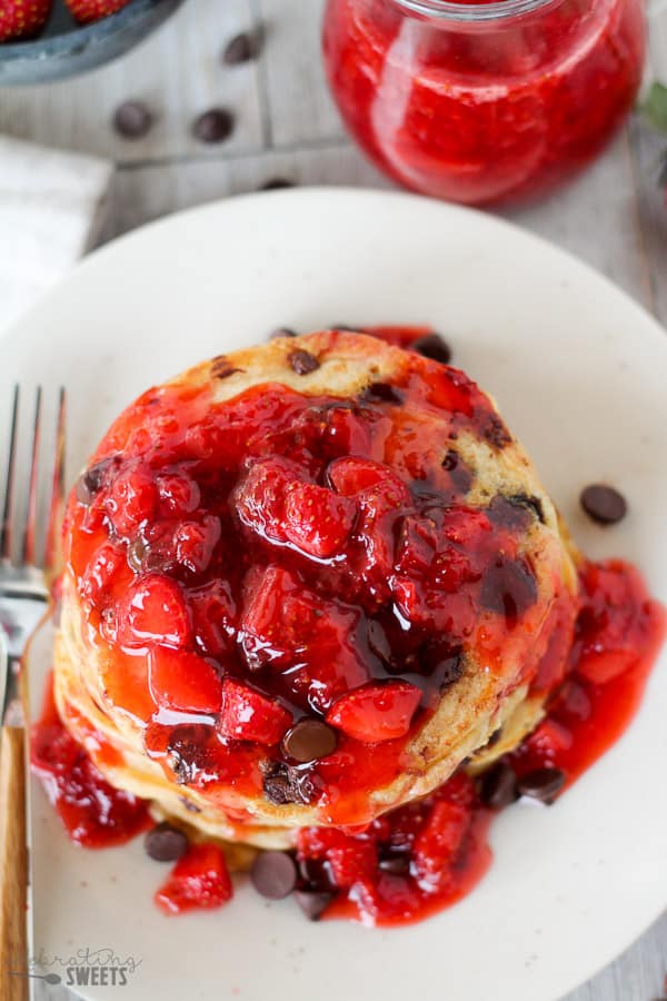 Stack of chocolate chip pancakes covered in strawberry syrup.