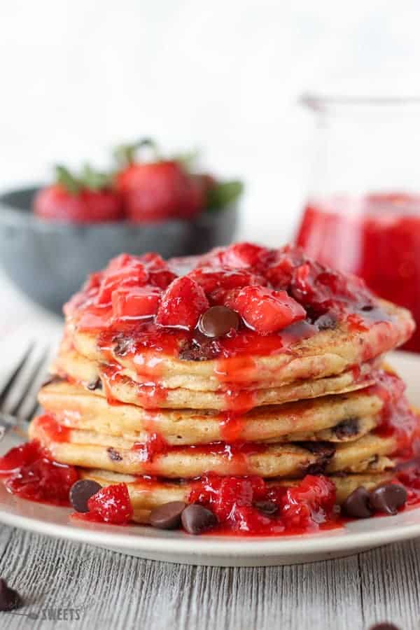 Stack of chocolate chip pancakes covered in strawberry syrup.