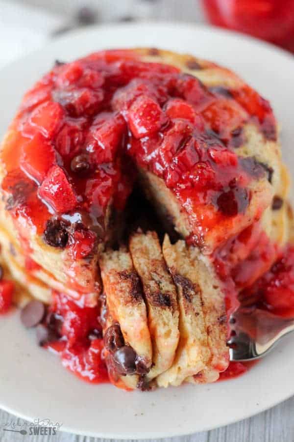 Stack of chocolate chip pancakes covered in strawberry syrup.