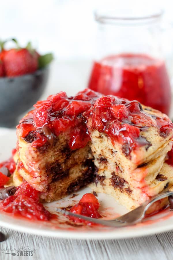 Stack of chocolate chip pancakes covered in strawberry syrup.