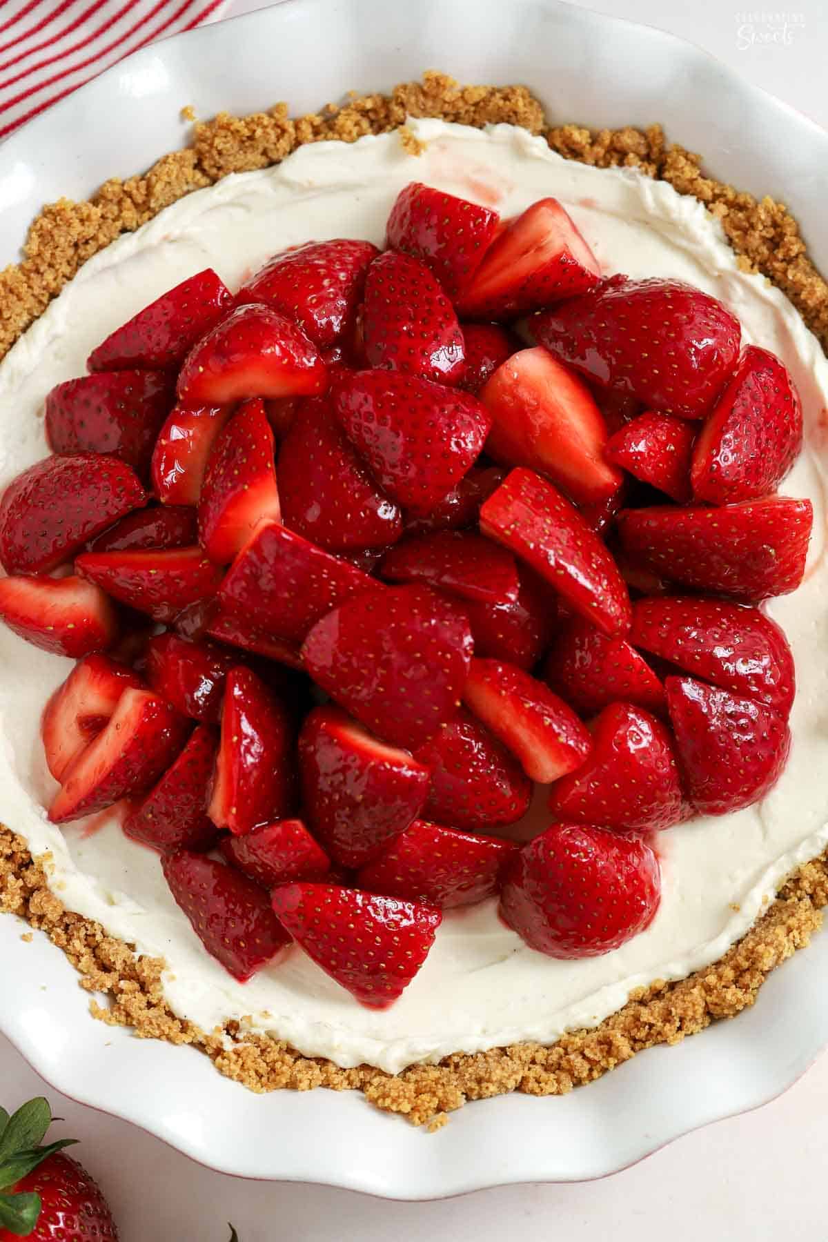 Strawberry cream cheese pie in a white pie plate next to a red and white striped napkin.