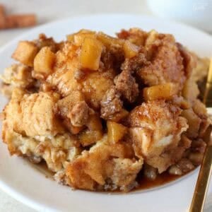 A serving of apple French toast casserole on a white plate with a gold fork.