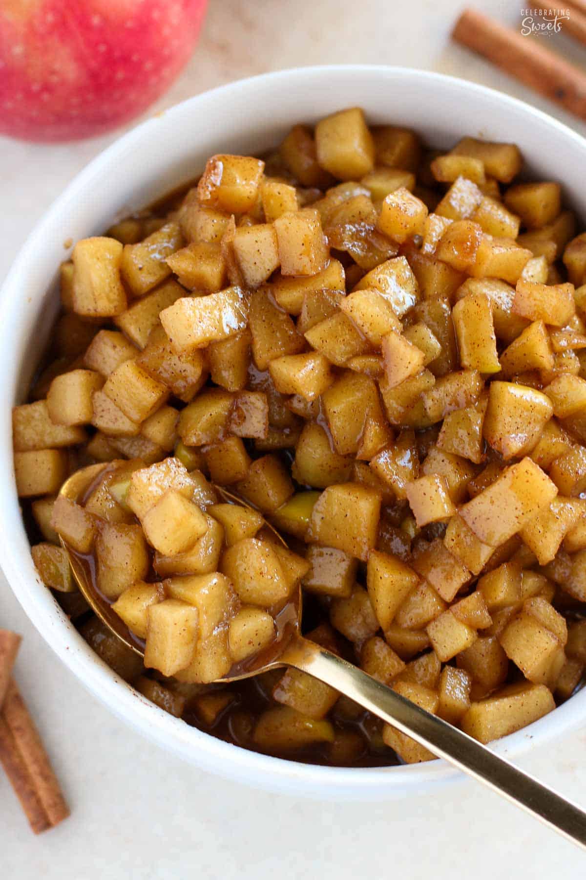 Diced apple compote in a white bowl with a gold spoon in it.