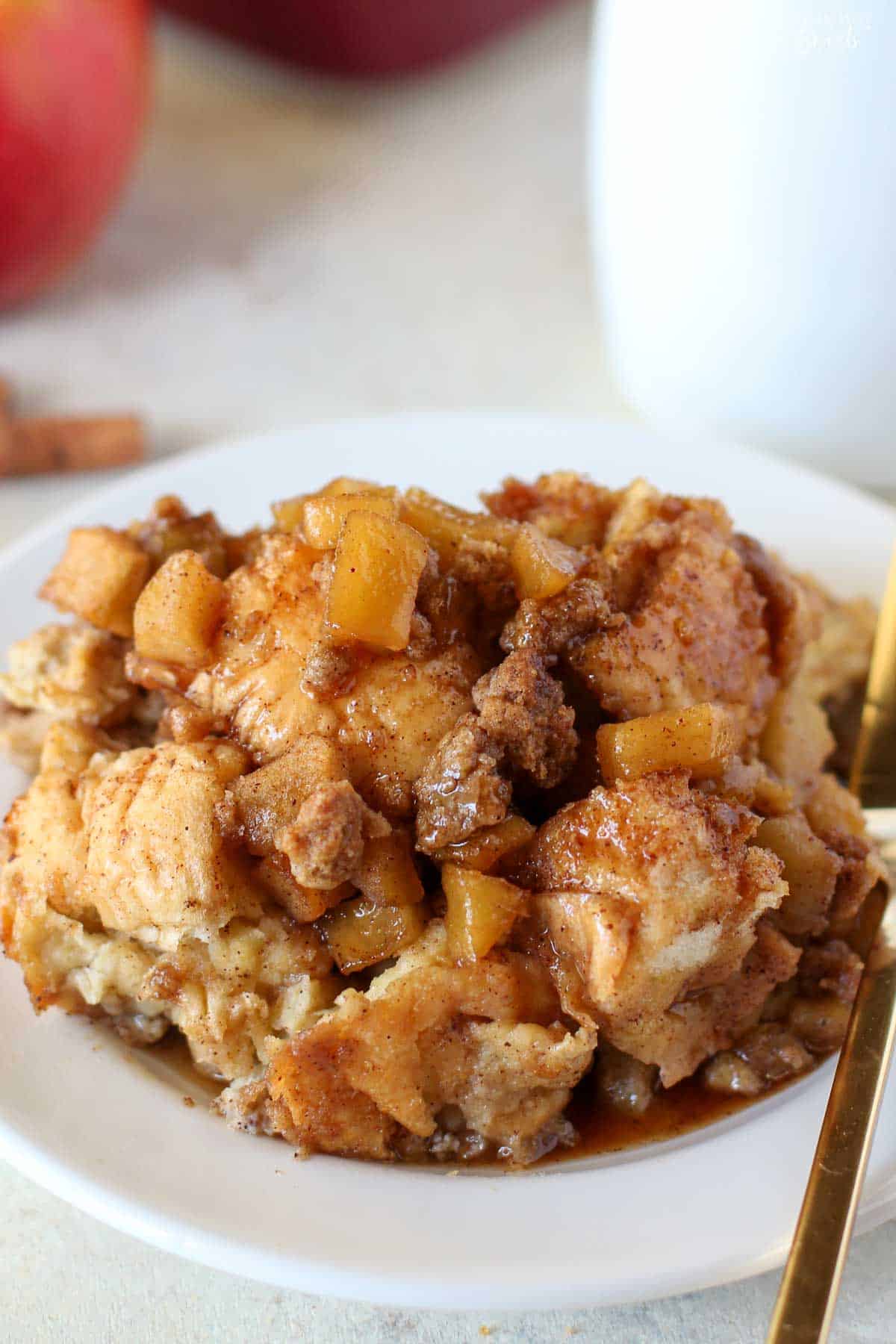 Apple French toast casserole on a white plate with a red apple in the background.
