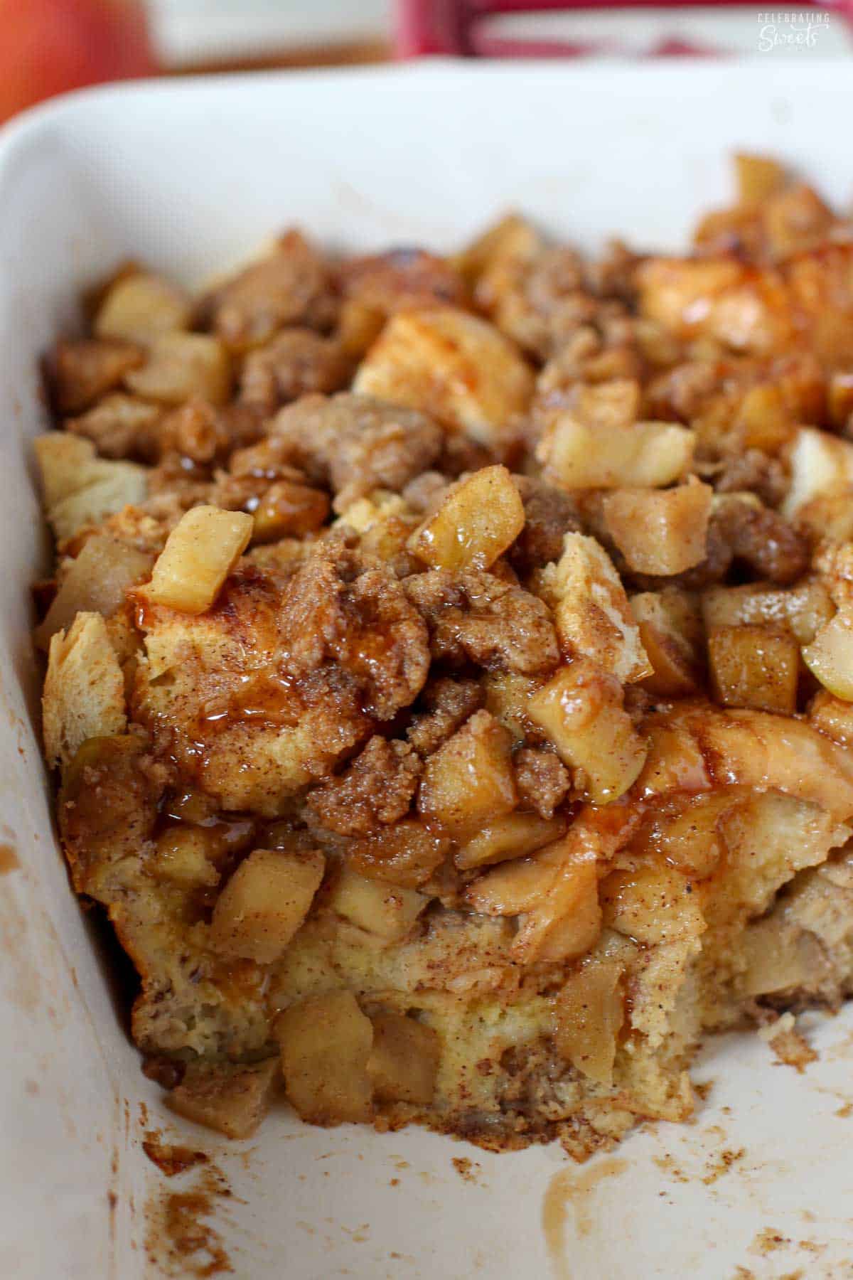 Close up of apple French toast casserole in a white baking dish with red handles.