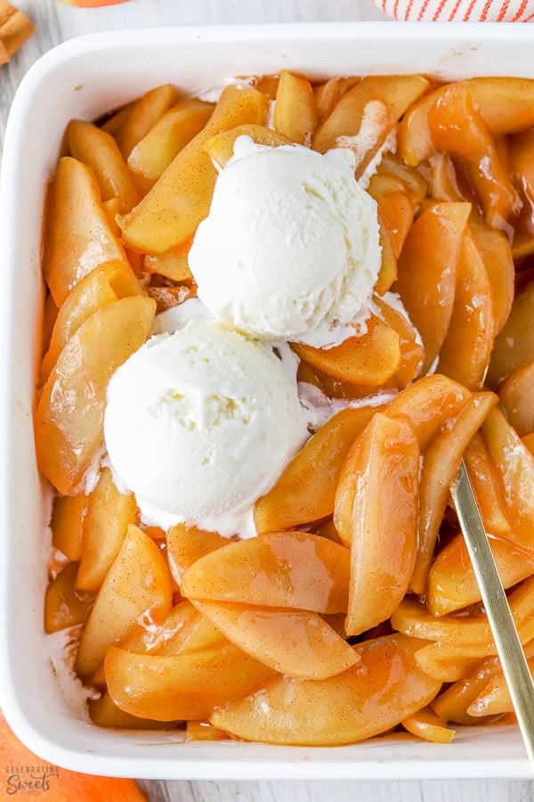 Cinnamon apples in a white baking dish topped with ice cream.