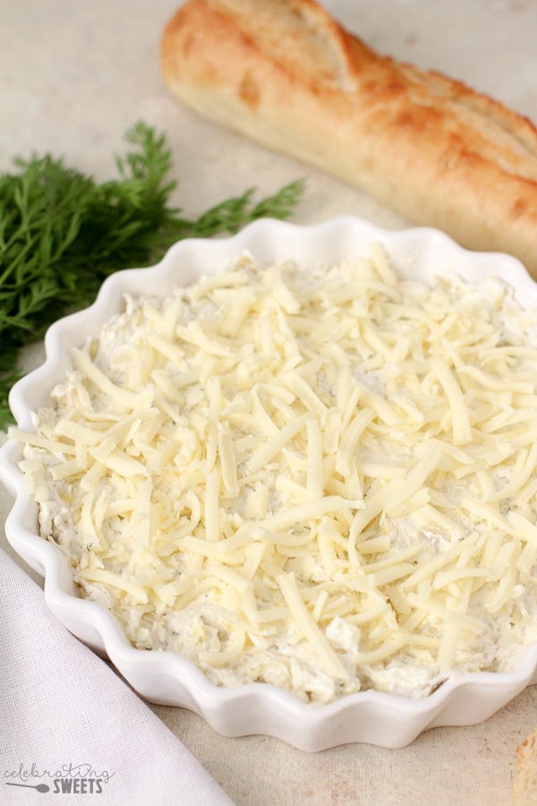 Artichoke dip in a white casserole dish topped with grated cheese