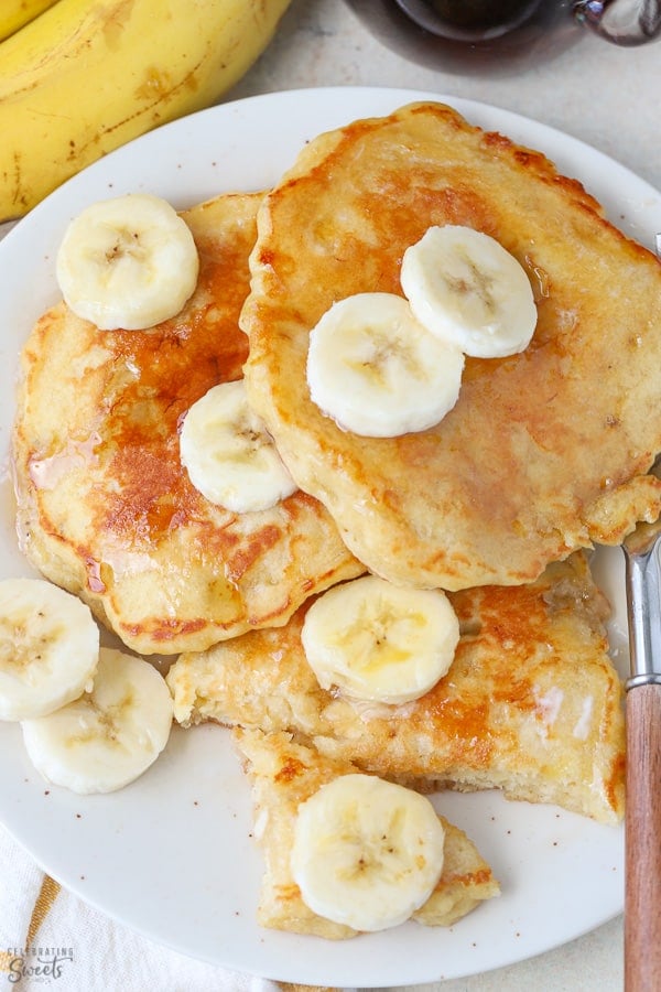 Banana pancakes on a white plate topped with sliced banana.