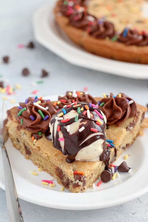Slice of cookie pie topped with vanilla ice cream, fudge sauce and sprinkles.