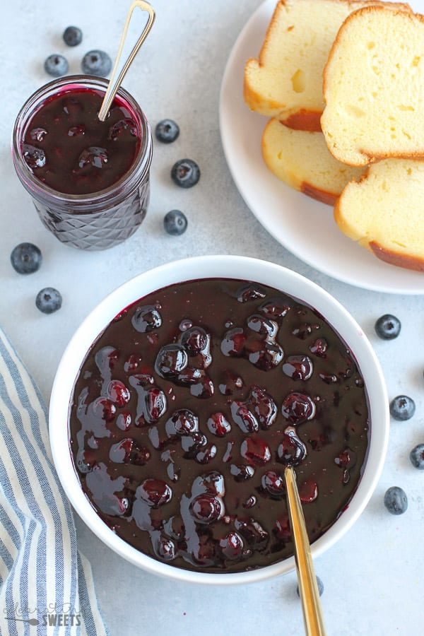 Blueberry Sauce in a White Bowl with Cake in the Background.
