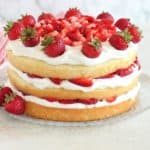 Three layers of cake filled with whipped cream and strawberries on a glass plate.