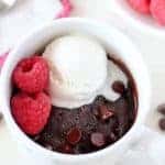 Brownie in a mug topped with vanilla ice cream and raspberries.
