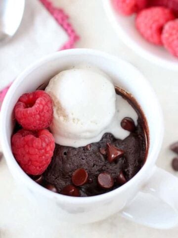 Brownie in a mug topped with vanilla ice cream and raspberries.