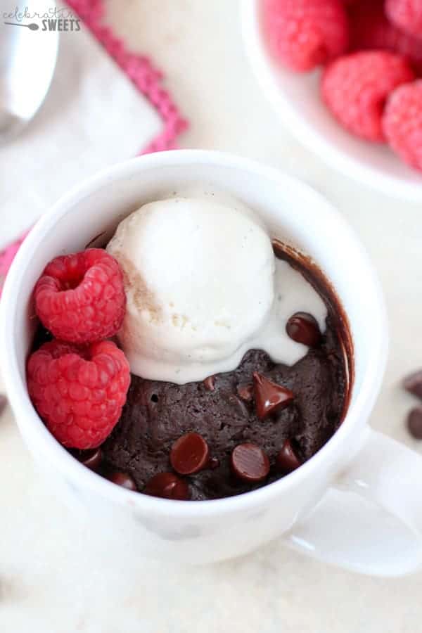 Brownie in a mug topped with vanilla ice cream and raspberries.