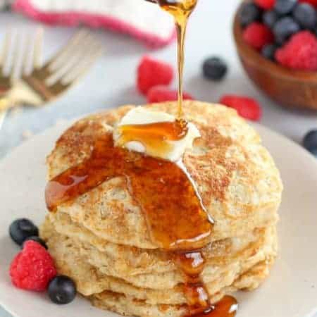 Syrup being poured over a stack of pancakes.
