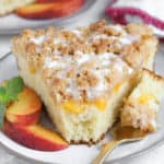 A slice of Peach Crumb Cake on a grey plate with peach slices.