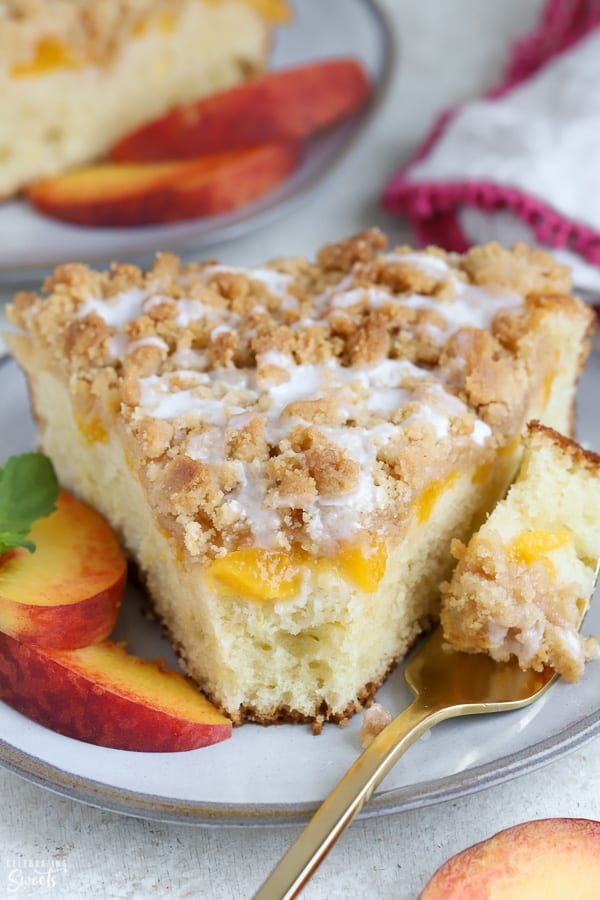 A slice of Peach Crumb Cake on a grey plate with peach slices. 