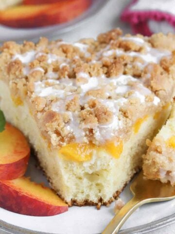 A slice of Peach Crumb Cake on a grey plate with peach slices.