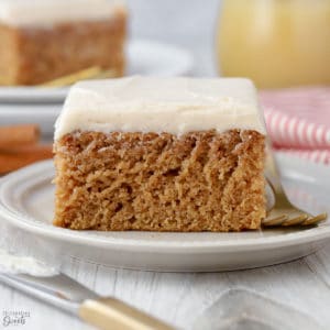 Slice of applesauce cake topped with frosting on a white plate.