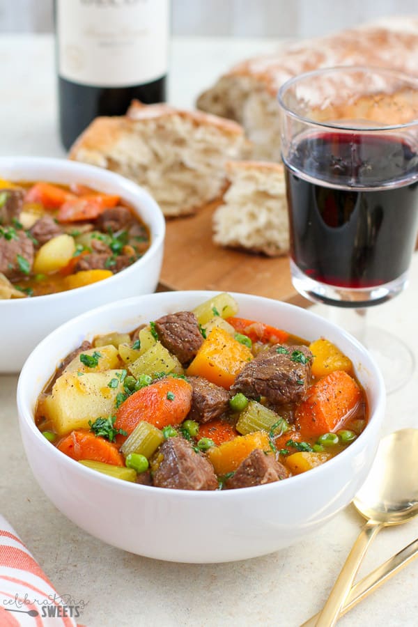 Beef stew and red wine with a loaf of bread in the background.