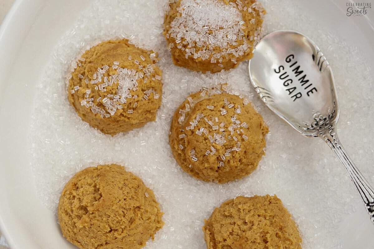 Ginger molasses cookie dough balls in a bowl of sugar.