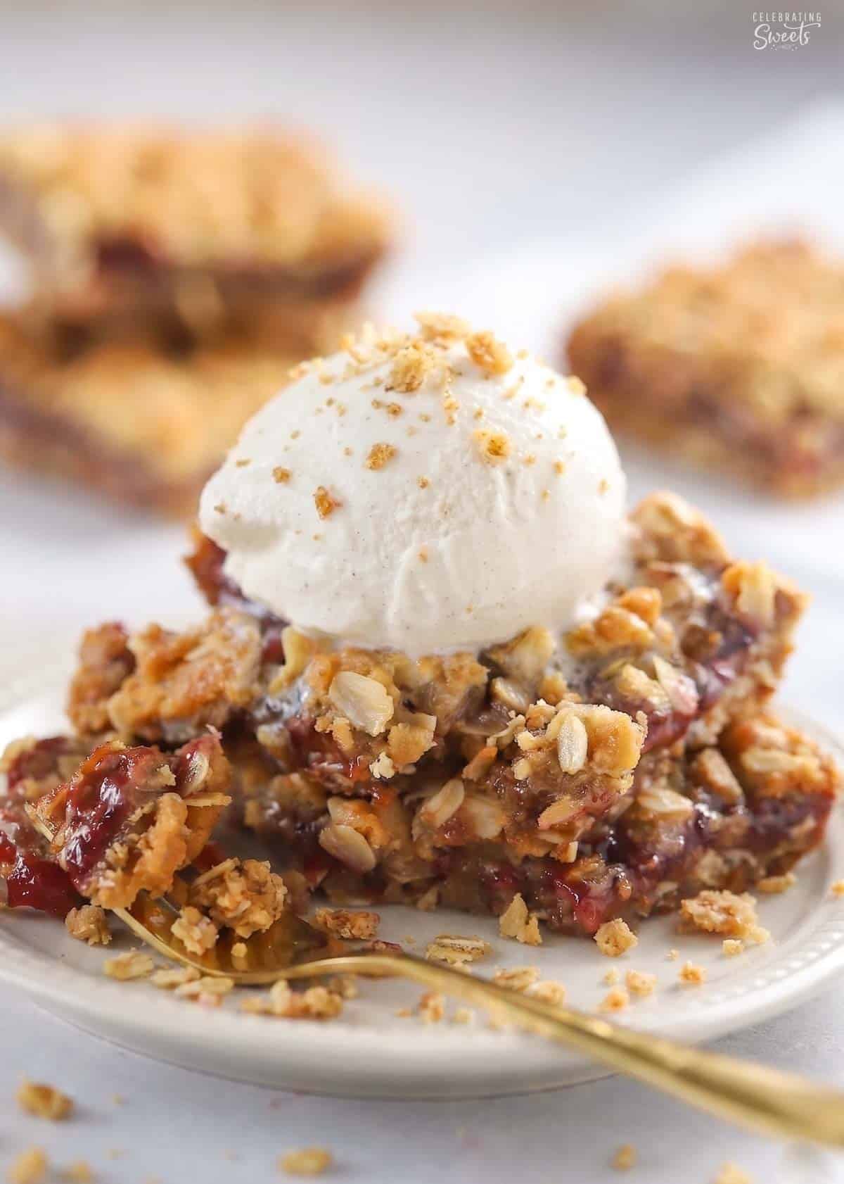 Two oatmeal jam bars topped with a scoop of vanilla ice cream on a grey plate.