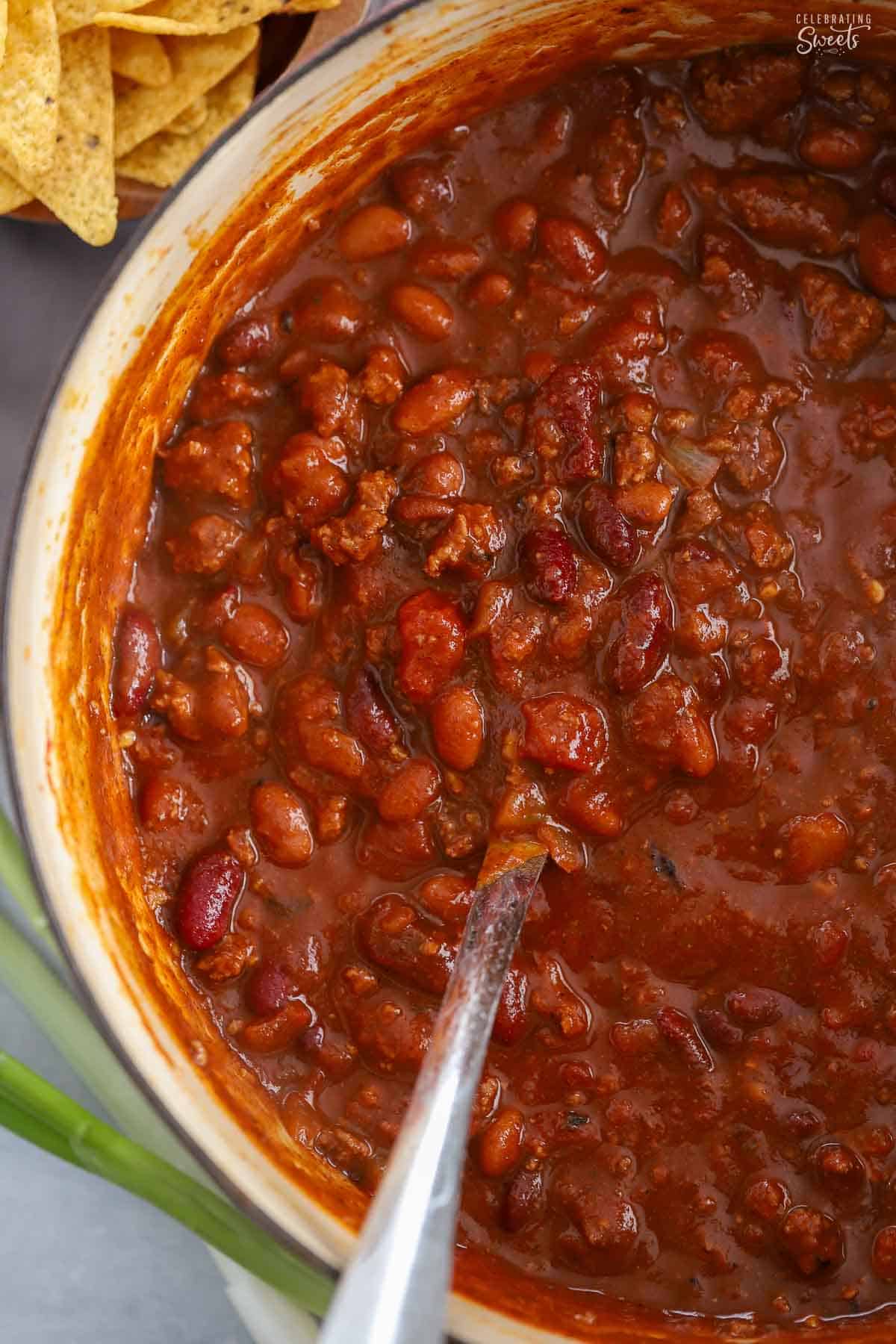 Beef chili in a dutch oven next to a bowl of tortilla chips.