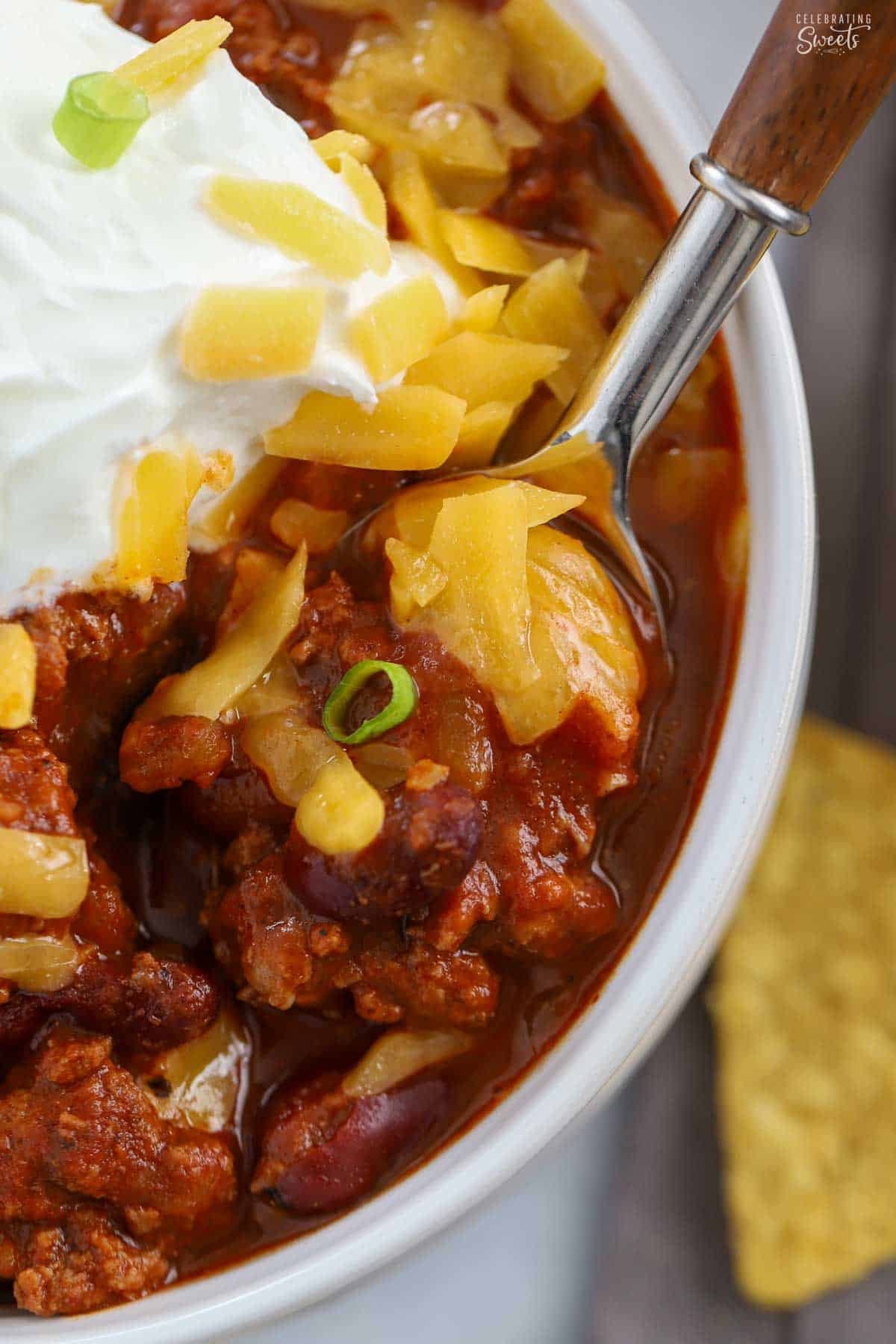 Closeup of beef chili on a spoon with shredded cheddar cheese.