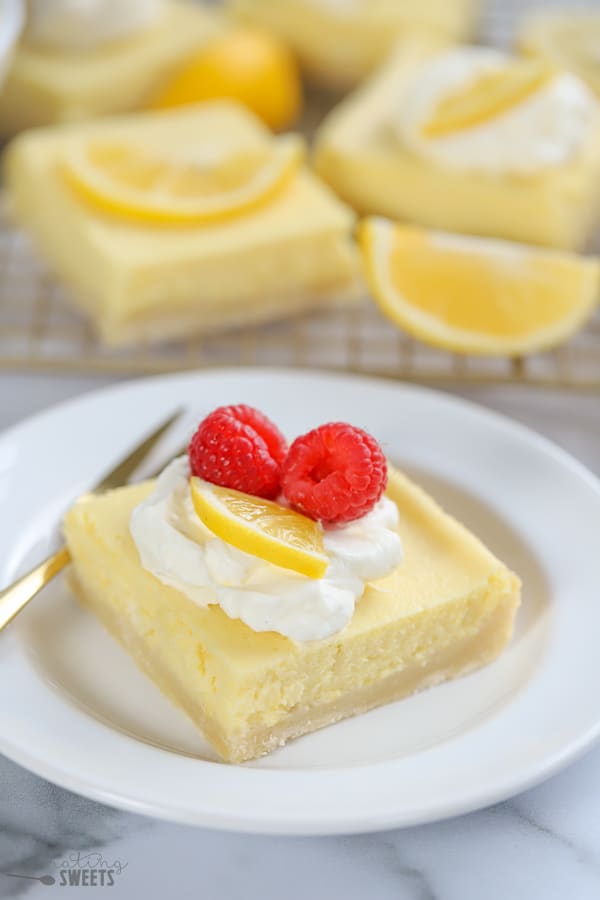 Lemon Bar on a white plate with whipped cream and a raspberry.