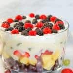 Layered fruit salad in a glass trifle dish topped with pudding and whipped cream.