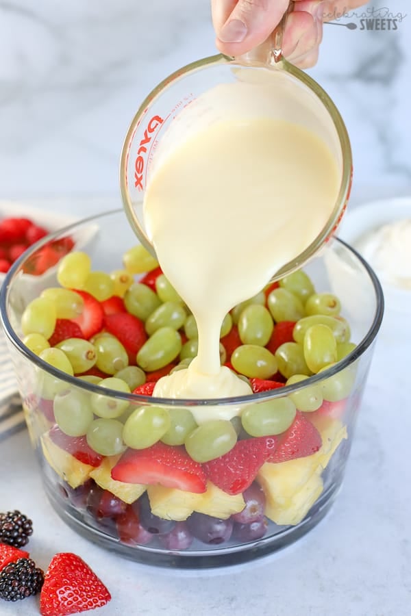 Layered fruit salad in a glass trifle dish with pudding on top.