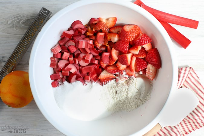 Ingredients for strawberry crisp in a large white bowl: strawberries, rhubarb, sugar, flour, orange zest.
