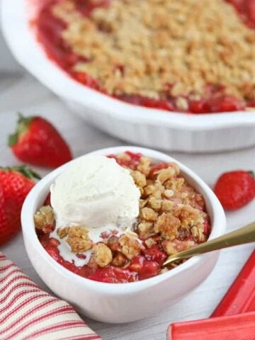 White bowl filled with strawberry rhubarb crisp topped with vanilla ice cream.