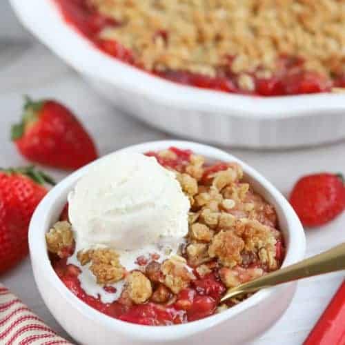 White bowl filled with strawberry rhubarb crisp topped with vanilla ice cream.