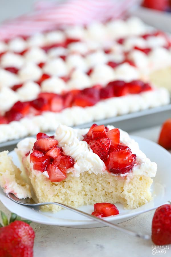 Slice of vanilla cake on a white plate topped with strawberries and vanilla frosting.