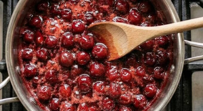 Cherry pie filling in a saucepan with a wooden spoon.