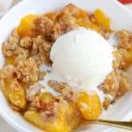 Peach crisp in a white bowl with a scoop of vanilla ice cream.
