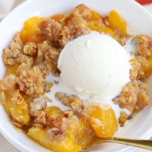 Peach crisp in a white bowl with a scoop of vanilla ice cream.