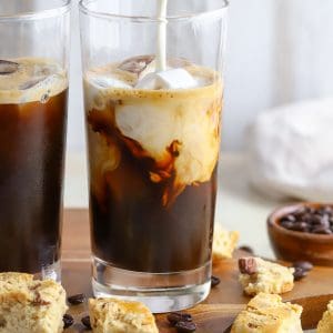 Zwei Gläser Eiskaffee mit Sahne, die hineingegossen wird.