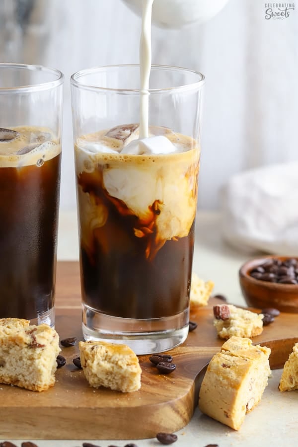 Two glasses of iced coffee with cream being poured in.