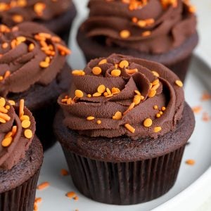 Chokolade cupcakes med chokolade frosting og orange drysser på en hvid plade.